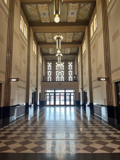 Tall hallway of the Durham Museum in Omaha. 
Doors under ornate windows and art deco chandeliers from the ceiling.