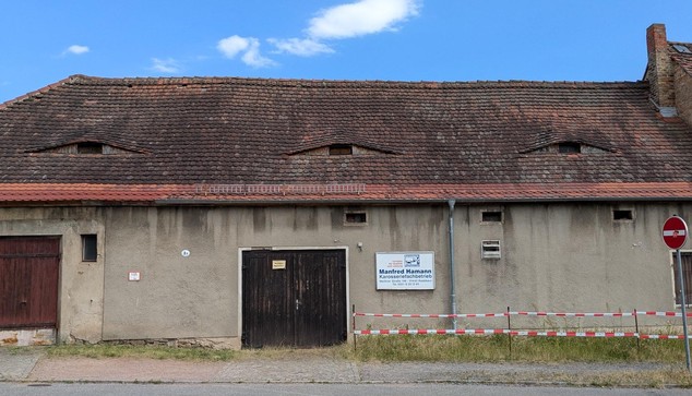 A red roofed building with three dormer windoes that look like eyes peering out of the roof.