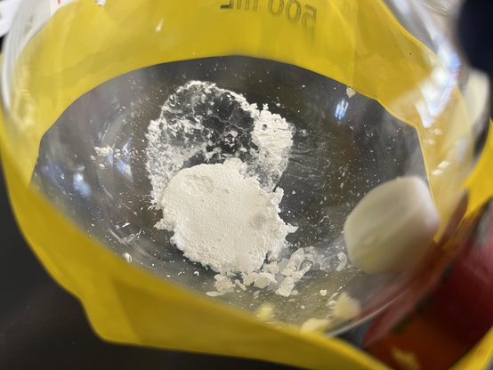 White powder at the bottom of a round bottomed flask. Stir bar taped to the side with yellow tape