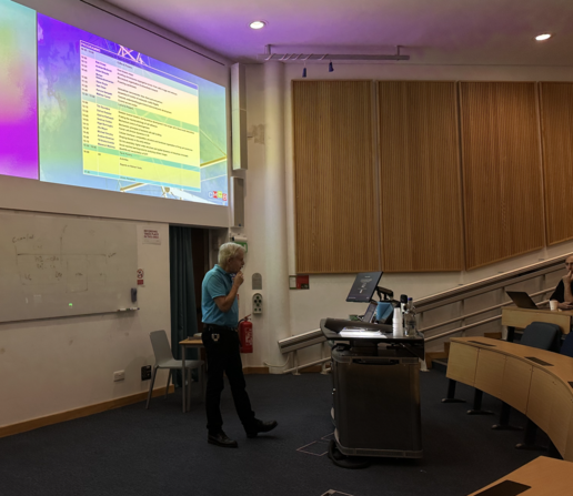 Rob Cross, standing in a darkened lecture theatre with a programme for the retreat showing on a large screen behind.