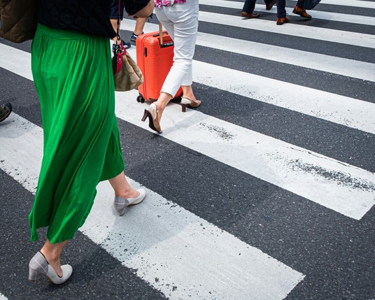 Person in a green skirt and pumps crossing a city street at a crosswalk.