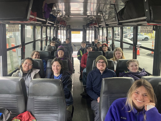 15 smiling university students sitting inside a school bus