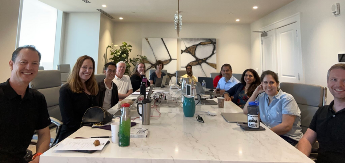 This image features MRRI Senior Staff and administrators sitting around a long rectangular conference table. The photo is taken from the head of the table, and everyone is looking at the camera and smiling.